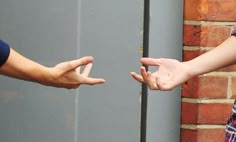 two people reaching out their hands towards each other in front of a brick wall and door