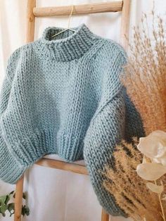 a blue knitted sweater sitting on top of a wooden chair next to dried flowers