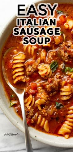 a white bowl filled with pasta and meat soup next to a spoon on top of a table