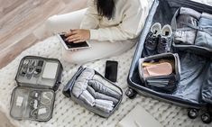 a woman sitting on the floor next to her suitcase with various items in it, all packed up