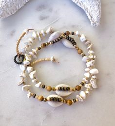 three bracelets with shells and beads on a marble table next to an ornament