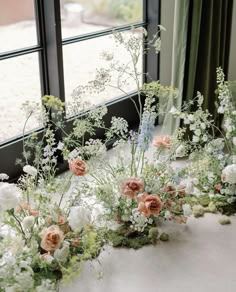 flowers and greenery are arranged in front of a window