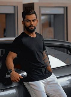 a man standing next to a car with his hand on the door handle and looking at the camera