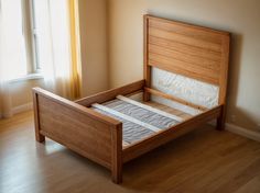 an empty bed frame in the corner of a room with wood floors and windows,