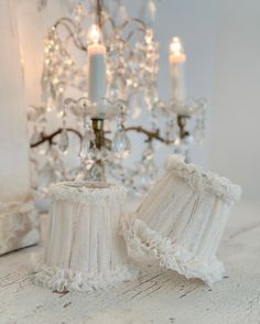 two white knitted lampshades next to a chandelier with candles in the background