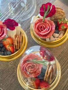 three bowls filled with food and flowers on top of a wooden table next to wine glasses