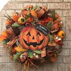 a wreath with a happy halloween sign hanging on the side of a brick wall next to leaves and pumpkins