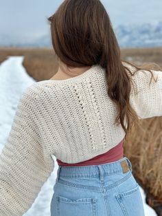 a woman standing in the middle of a field wearing a sweater and jean shorts with her back to the camera