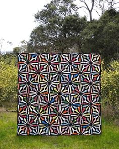 a large quilt sitting on top of a lush green field next to tall grass and trees