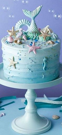 there is a blue cake with stars and mermaid decorations on the top, sitting on a white pedestal