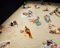 many people are laying on the sand and sunbathing at the beach while one person is taking a photo