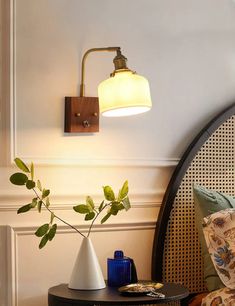 a lamp that is on the side of a bed next to a table with a plant