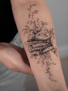 a woman's arm with a stack of books and flowers tattoo on her left forearm