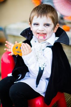 a young boy dressed as dracula sitting on top of a red chair