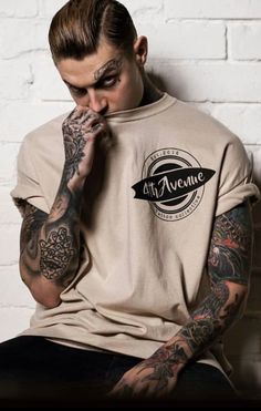 a man with tattoos on his arms and shoulder sitting against a white brick wall wearing a t - shirt that says eat awesome