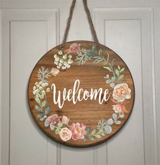 a welcome sign hanging on the front door with flowers and leaves painted all over it