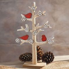 a small wooden christmas tree with red birds on it and pine cones in the background