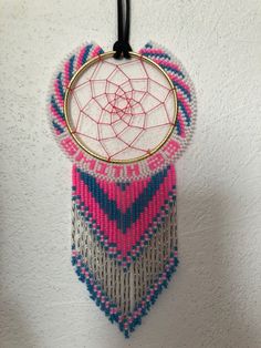 a pink and blue beaded dream catcher hanging from a hook on a white wall