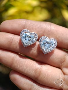 two heart shaped diamond earrings are shown on someone's hand