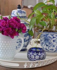 purple flowers in blue and white vases sitting on a tray with two teapots