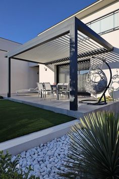 a modern house with grass and rocks in the front yard, as well as an outdoor dining area