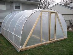 a small greenhouse with plastic covering on the roof and side walls, in front of a house