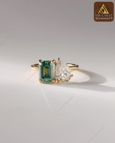 an emerald and diamond ring with two pear shaped diamonds in the middle, on a white background