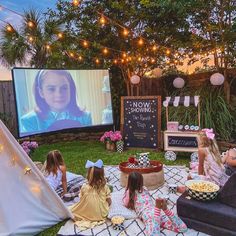 some kids are sitting on the grass and watching movies in front of a teepee tent