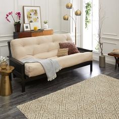 a living room with white walls and wood flooring on the wooden floor, beige futon