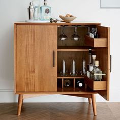 a wooden cabinet with wine glasses and liquor bottles in the bottom section, on top of a hard wood floor