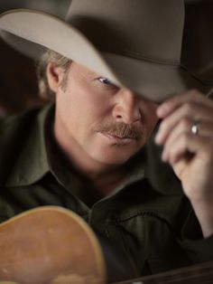 a man wearing a cowboy hat and holding a guitar in his right hand while looking into the distance