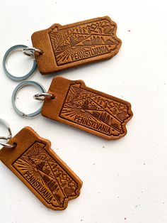 two leather keychains with mountains and trees engraved on the front, one is brown