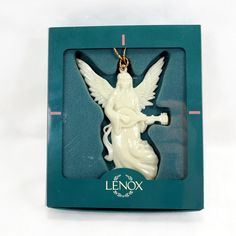 a white angel ornament in a green box with a gold chain hanging from it's side