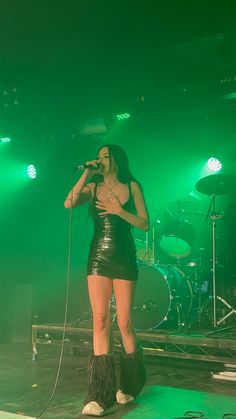 a woman in a leather outfit singing into a microphone on stage with green lights behind her