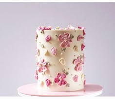 a white and pink cake with flowers on the frosting is sitting on a plate