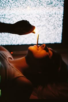 a woman laying down with a lit match in her mouth next to a flat screen tv