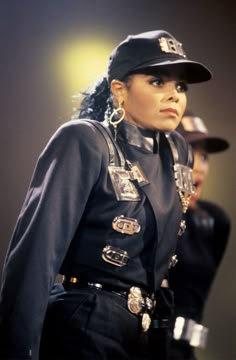 a woman in uniform standing on stage with other people behind her and one person wearing a hat