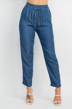 A pair of denim jogger pants featuring a high-rise elastic waistband, relaxed fit, cuffed hem, waistband, self-tie drawstring, pockets, and a full length. Fabric: 100% LYOCELL Made in Egypt Spring Utility Jeans With Elastic Waistband, Spring Cropped Leg Cargo Jeans With Relaxed Fit, Spring Cargo Jeans With Relaxed Fit And Cropped Leg, Spring Relaxed Fit Cropped Cargo Jeans, Trendy Relaxed Fit Bottoms With Tie Waist, Spring Cropped Leg Relaxed Fit Cargo Jeans, Trendy Bottoms With Tie Waist And Relaxed Fit, Relaxed Fit Tapered Leg Bottoms With Tie Waist, Summer Relaxed Fit Cargo Jeans With Elastic Waistband