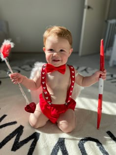 a baby in a red bodysuit holding a toothbrush and wearing a red bow tie