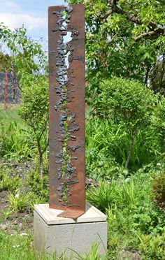 a tall metal sculpture sitting in the middle of a lush green field