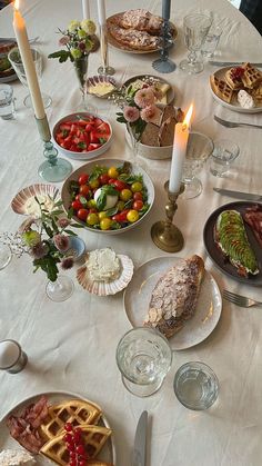 a white table topped with plates and bowls filled with food next to candles on top of a table