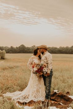 a bride and groom are standing in the middle of a field with tall grass, wearing cowboy hats