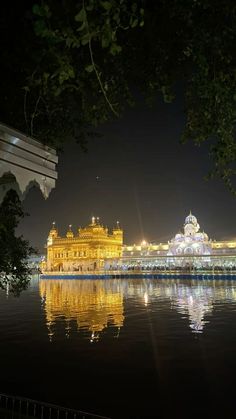 the golden building is lit up at night by the water's edge with lights reflecting in the water