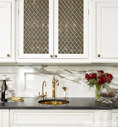 a kitchen with white cabinets and marble counter tops, gold faucet sink and wine glasses on the counter