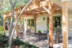 a covered patio with table and chairs under a wooden pergolated arbor on the side of a house