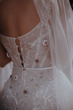 the back of a woman's wedding dress with flowers on it and veil over her shoulder