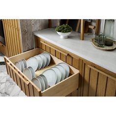 an open drawer in a kitchen filled with white plates and cups on top of a counter