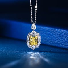 a fancy yellow diamond necklace on a blue surface with diamonds around the pendant and chain