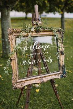 an easel with a sign that says welcome to the wedding and is decorated with greenery