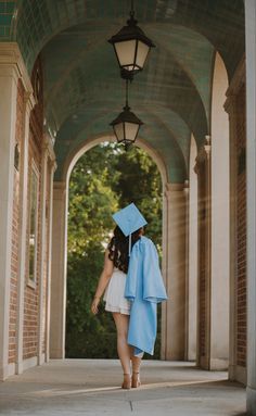 a woman in a graduation gown and cap walks under an archway with a light blue robe on